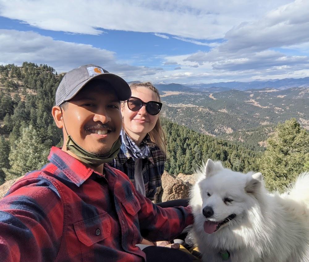 Rus Pascual and his wife with their dog atop a mountain with a wide view of a mountainous valley below