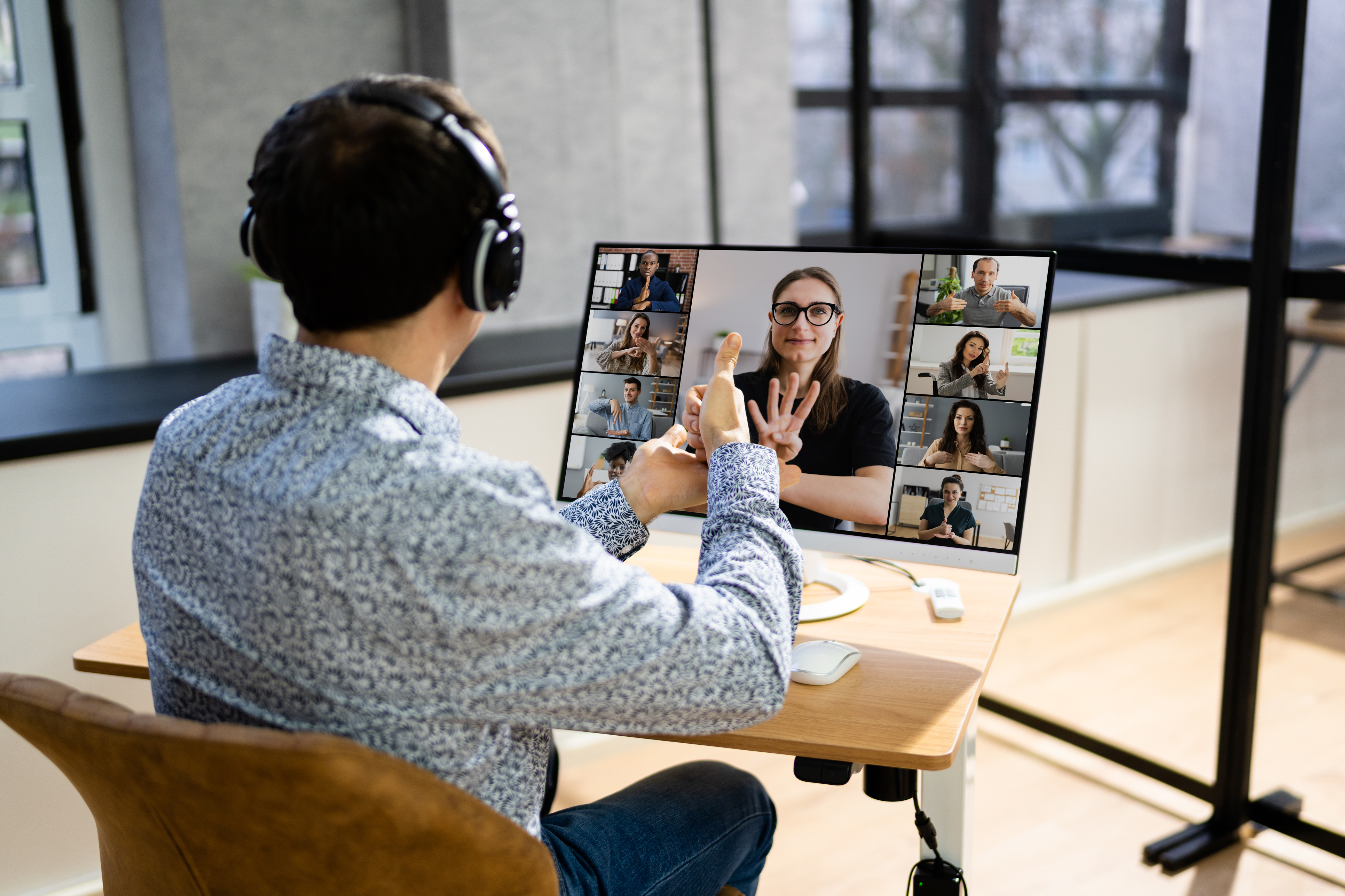 A man uses sign language on a virtual work meeting on a laptop. Several coworkers displayed on the computer screen are also signing