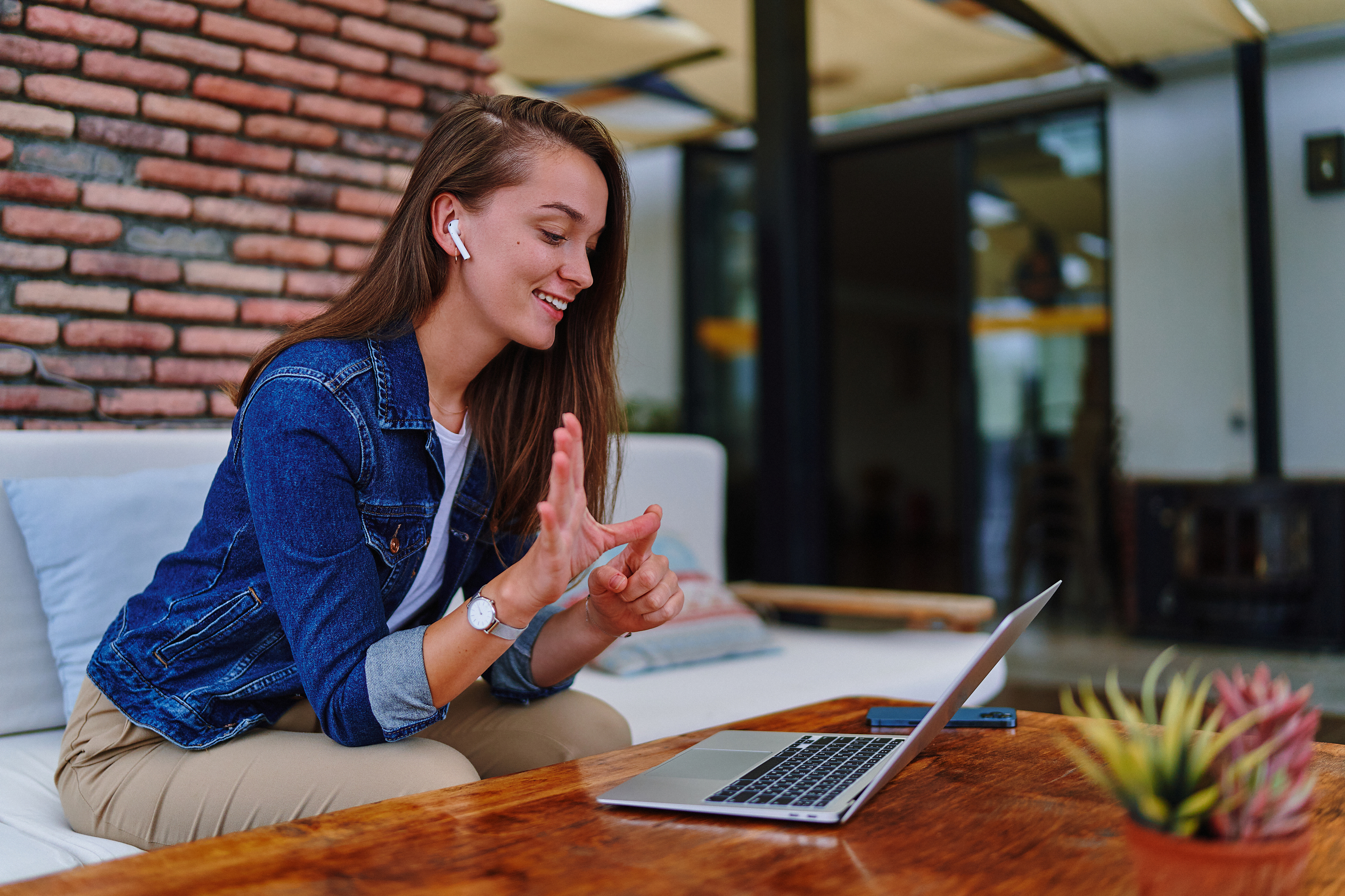 Woman uses sign language and smiles in front of an open laptop on a sofa in a cafe