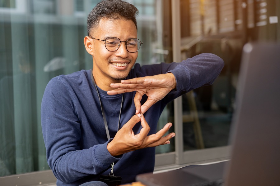 Man uses sign language and smiles in front of an open laptop