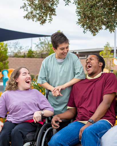 A group of people with varied abilities relaxing in a park and laughing as though they just heard a joke.