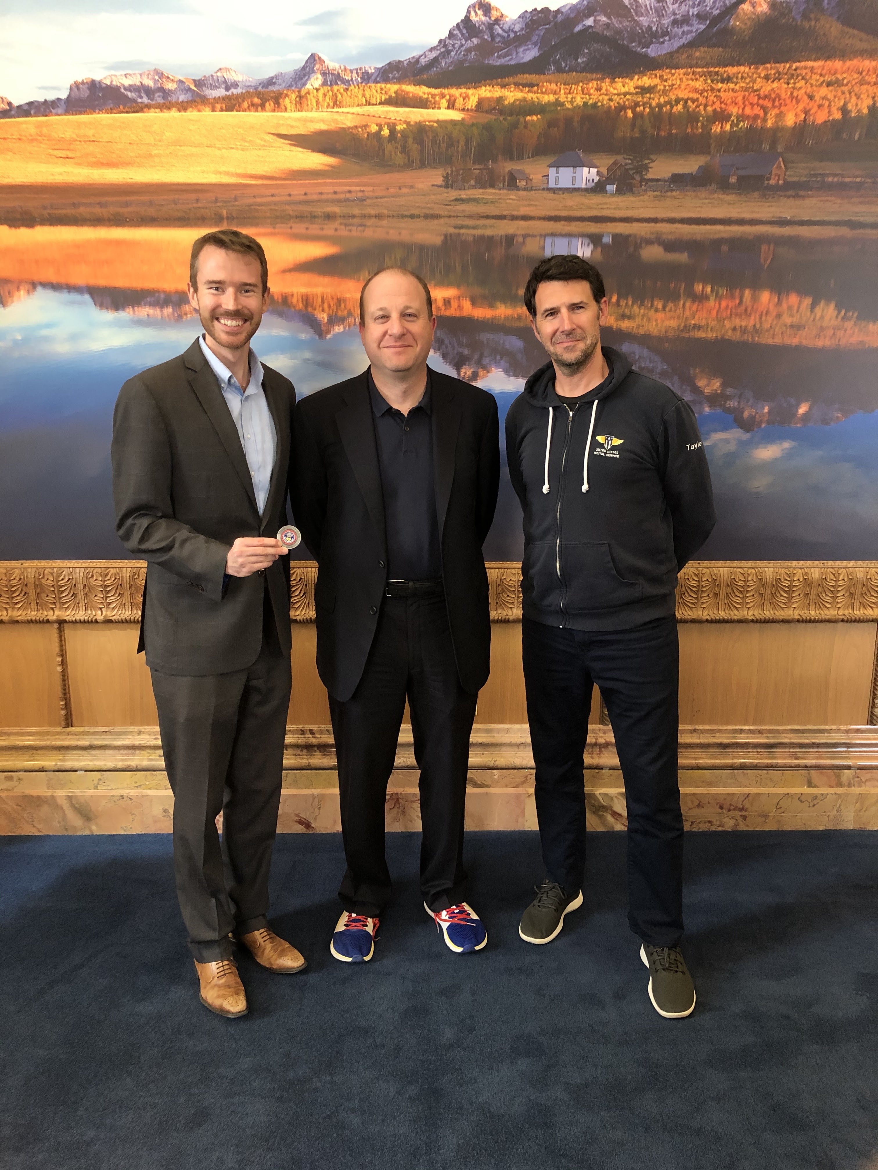 Photo of three individuals standing in front of a picture of mountains