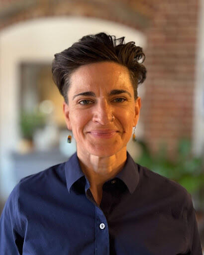 Woman with short dark hair wearing a dark blue button down shirt smiling. 