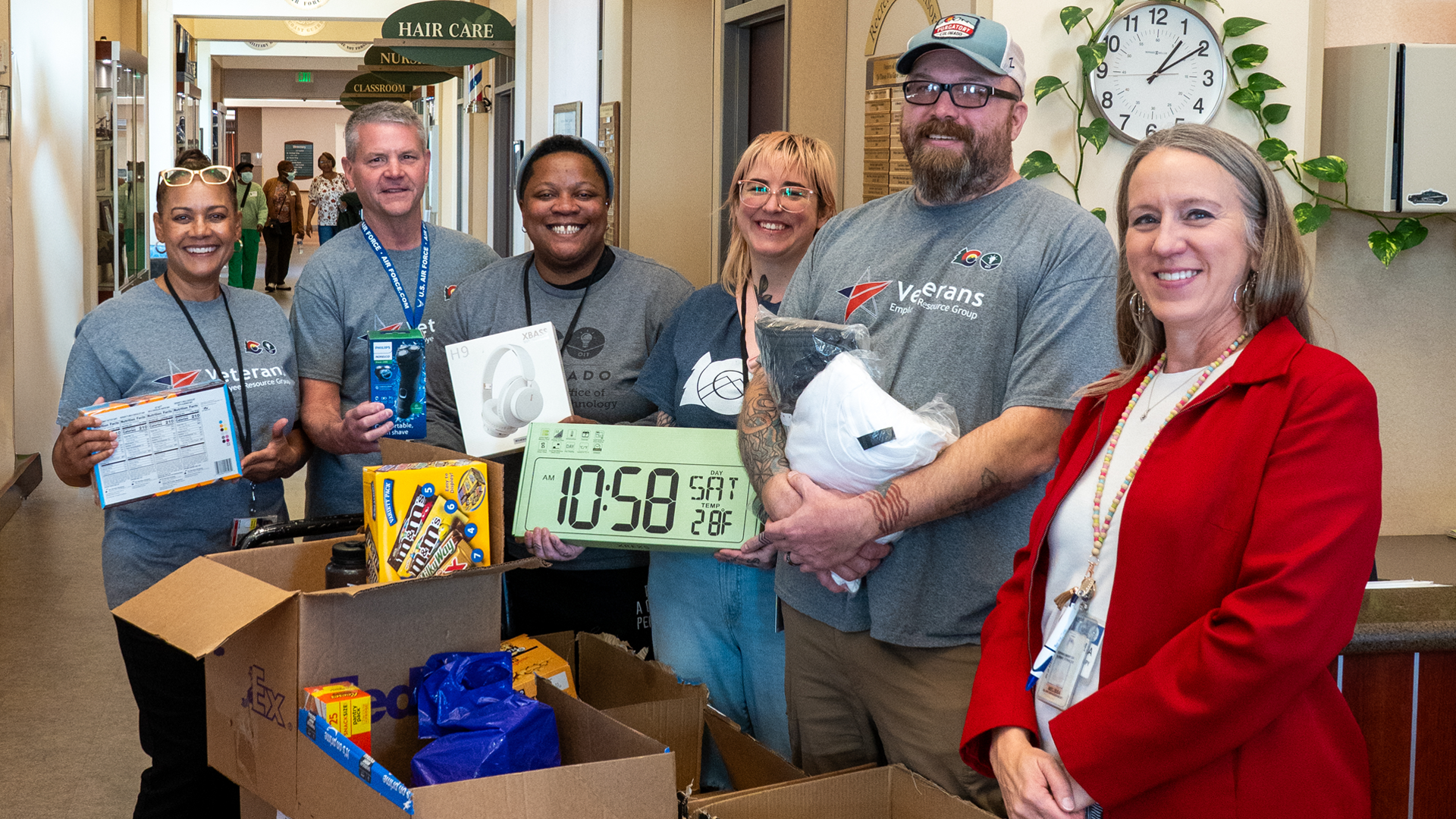 Group of OIT employees holding signs standing in front of donation boxes full of cloths and goods. 