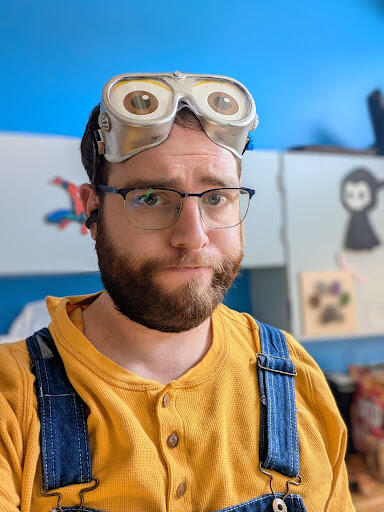 Man with brown hair and a beard wearing glasses and a minion costume. 