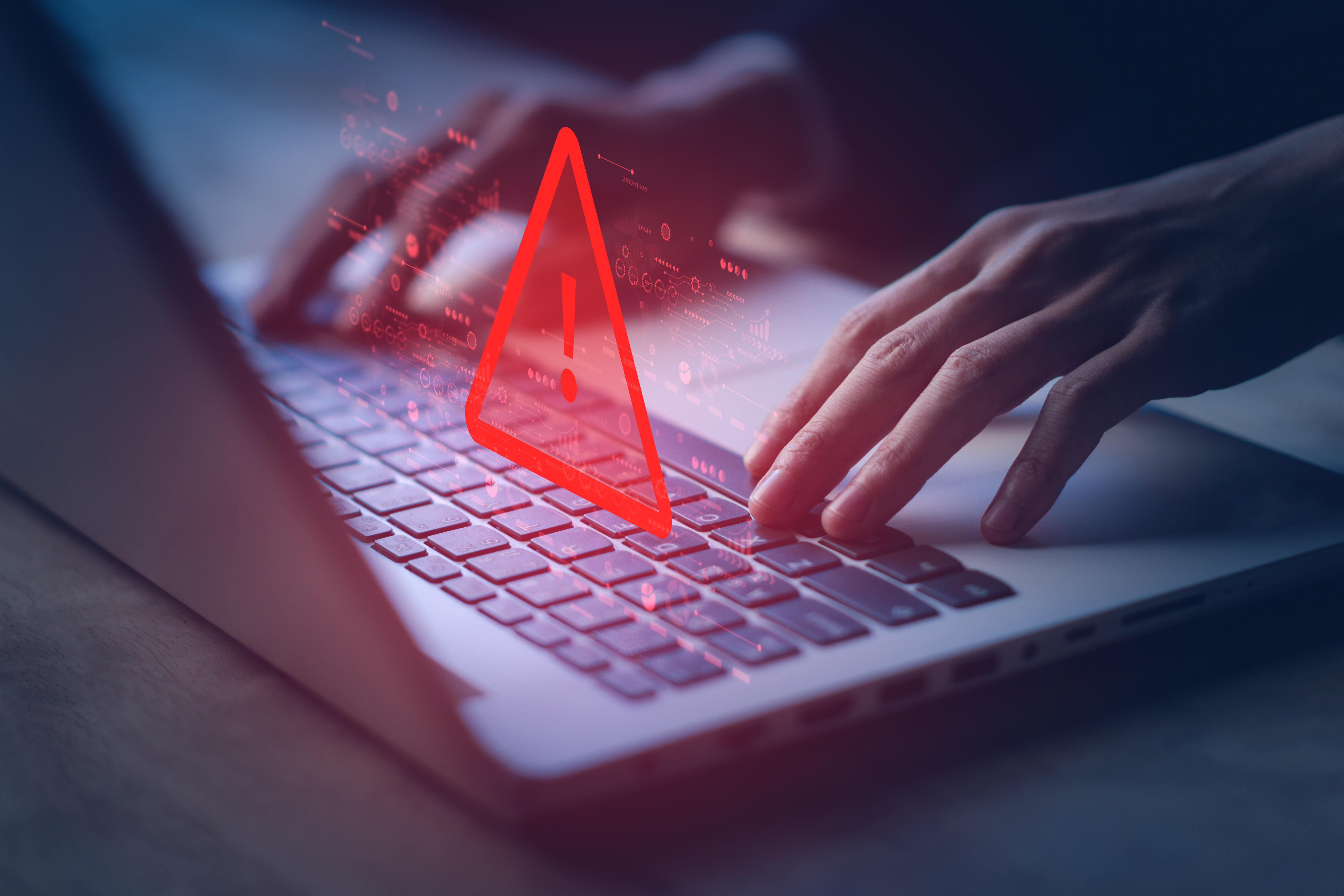 Hands typing on a laptop with a red warning symbol in front