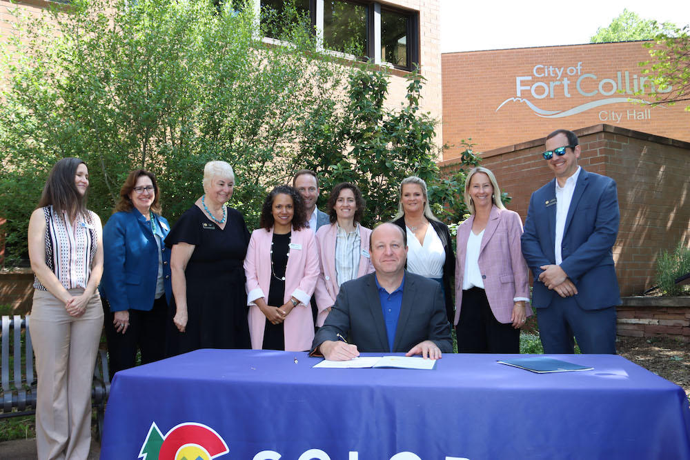 Governor Polis signs a bill with OIT and Colorado Broadband Office staff behind him