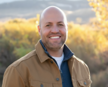 Man standing outside in rugged autumn attire with a blurred scenic mountain background.