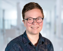 Woman with short hair wearing glasses and a blue shirt sitting in an office smiling. 