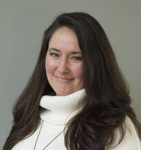 Katie Shakun sitting in white turtle neck smiling. 