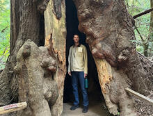 Grant Smith standing at the base of a tree in wearing blue jeans.