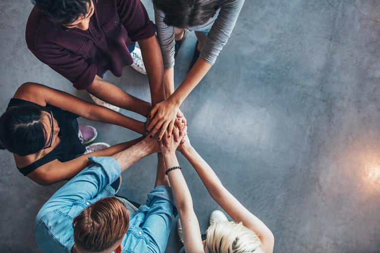 Several people in a circle with their hands clasped indicating teamwork